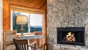 A cozy room with a stone fireplace, a wooden desk, wicker chairs, and a lamp.