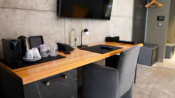 A modern hotel room with a wooden desk, a flat-screen TV, a coffee maker, a phone, and a remote control.