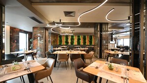 A modern restaurant interior with wooden tables and chairs, a green vertical garden wall, and contemporary lighting fixtures. - Aniroc Signature Hotel (Arad)