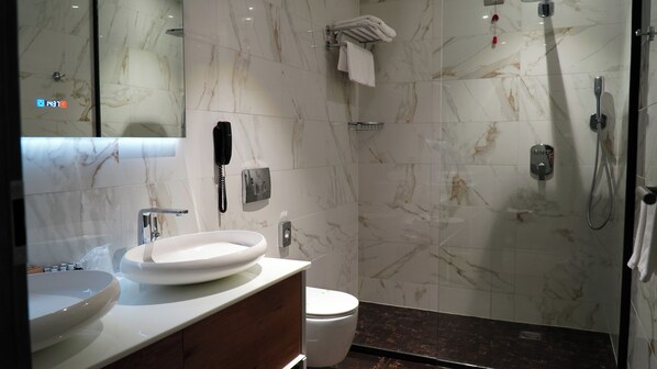 Un baño moderno con tocador de mármol, inodoro, ducha y zona de ducha con cerramiento de vidrio.