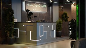 A modern reception desk with a neon sign, potted plants, and a minimalist design. - Aniroc Signature Hotel (Arad)