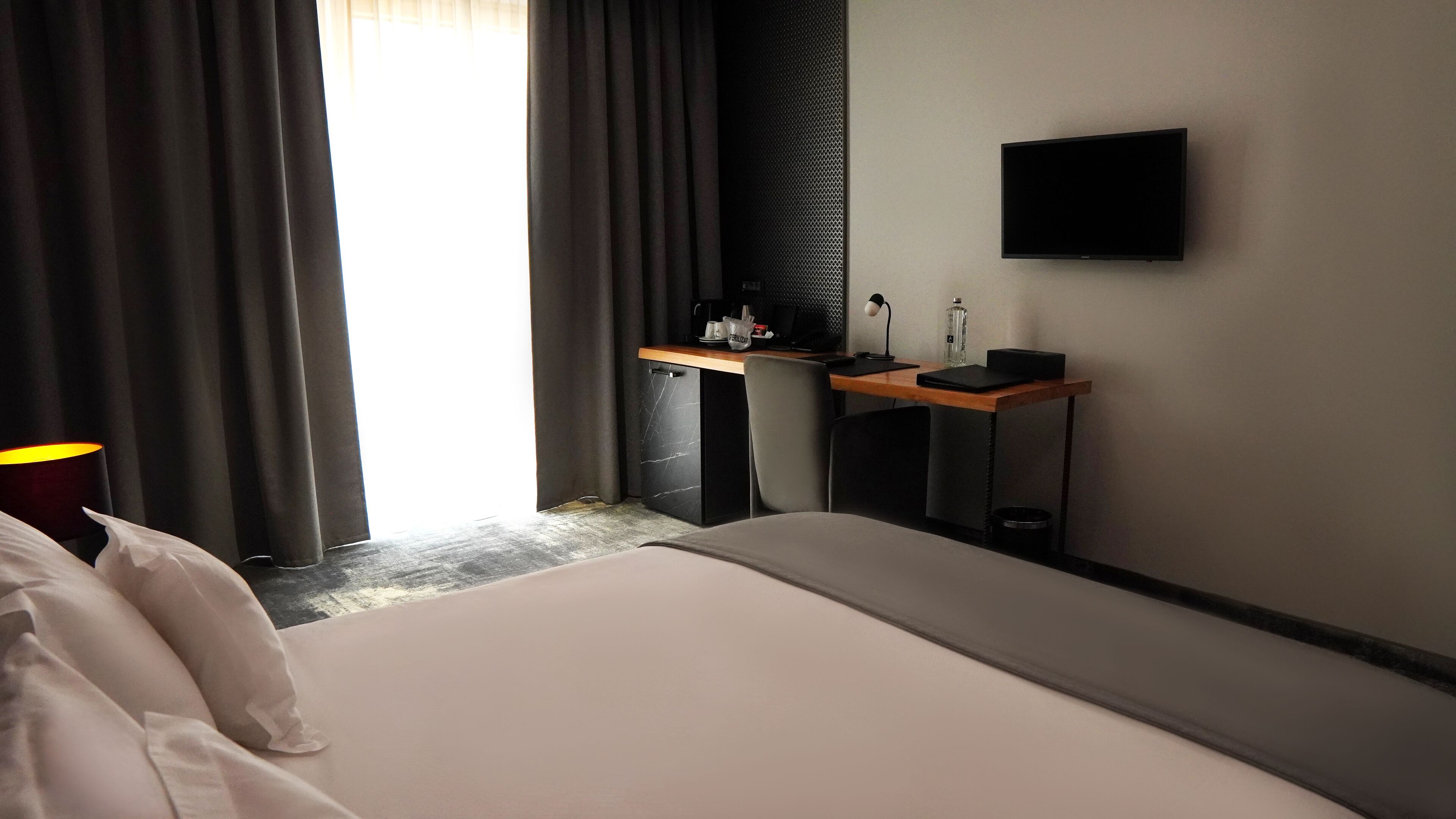A hotel room with a bed, a desk, a chair, a TV, and a window with curtains.