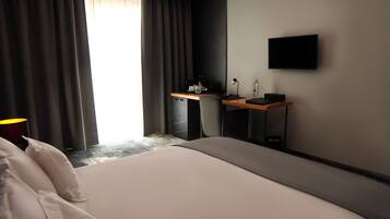 A hotel room with a bed, a desk, a chair, a TV, and a window with curtains.