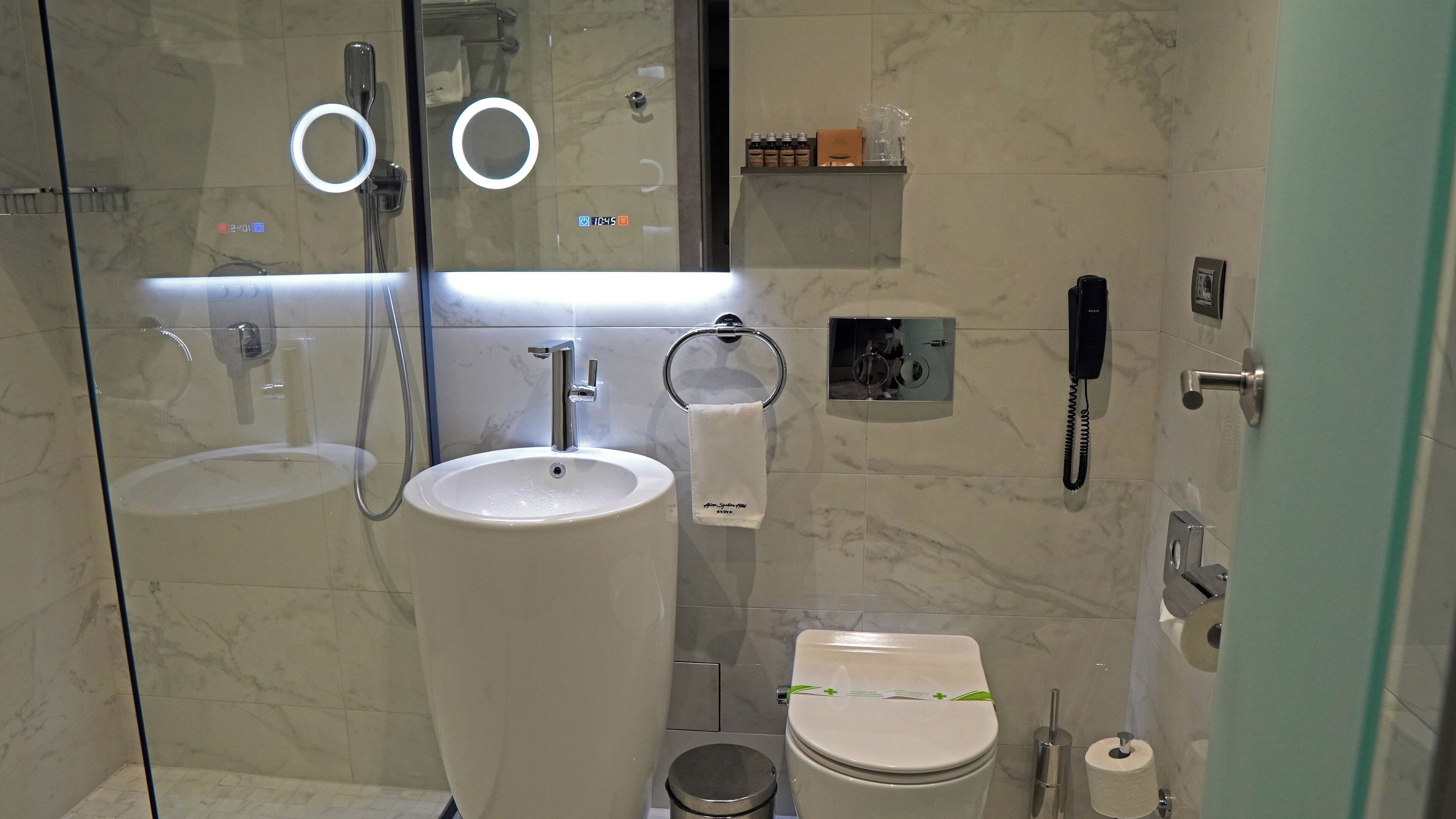 Un baño moderno con ducha envuelta en vidrio, un lavamanos grande, un inodoro y un teléfono.