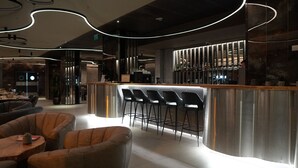 A modern bar area with a curved bar, bar stools, and a seating area with cushioned chairs. - Aniroc Signature Hotel (Arad)