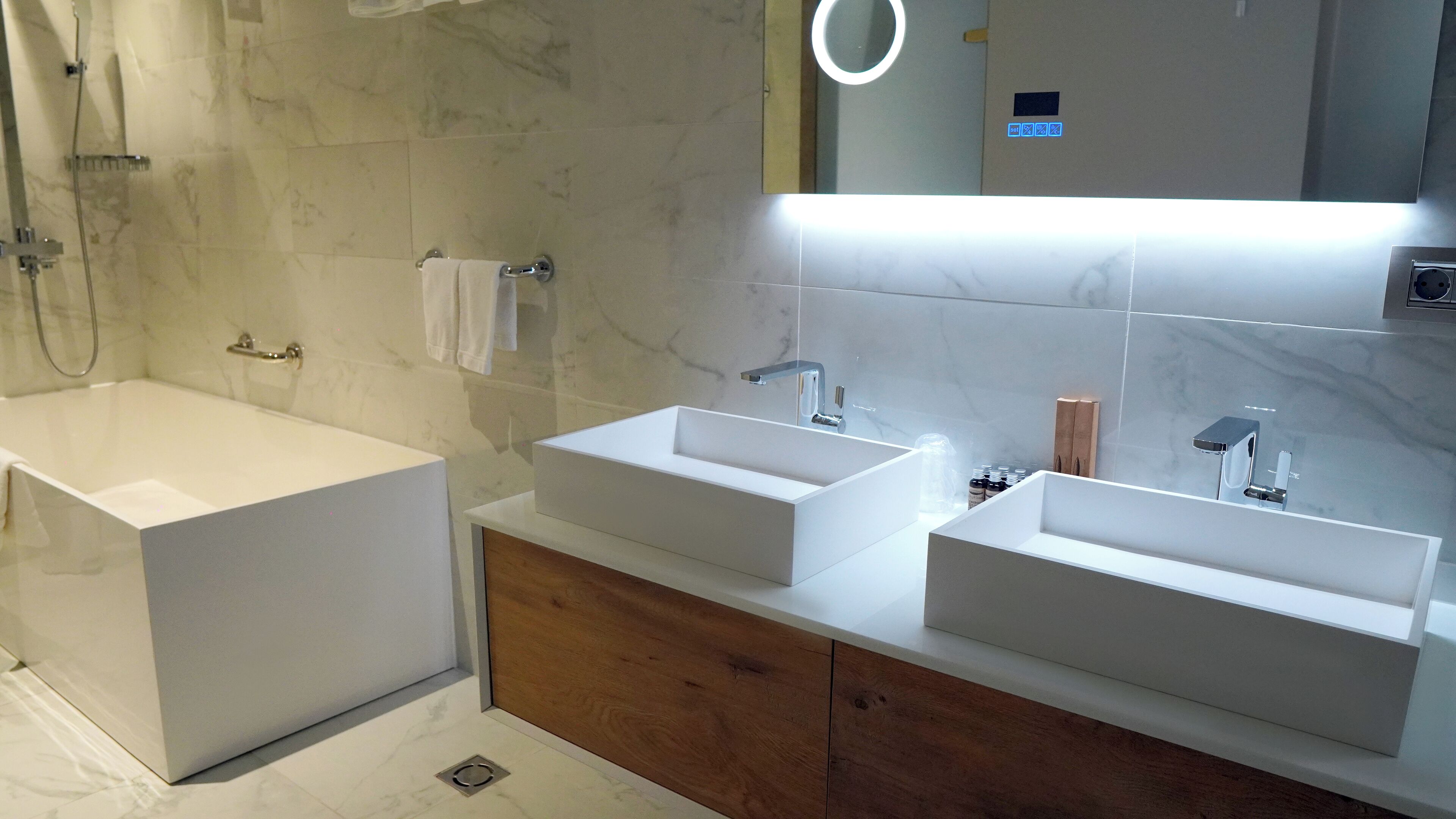 Un baño moderno con una bañera grande, dos lavamanos y un espejo con luz superior.