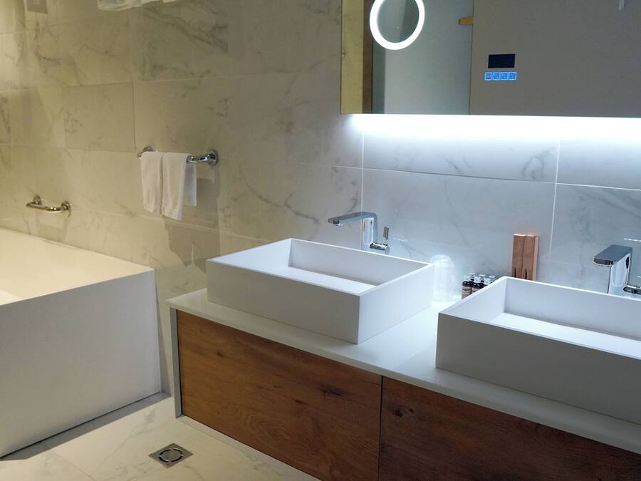 Un baño moderno con una bañera grande, dos lavamanos y un espejo con luz superior.