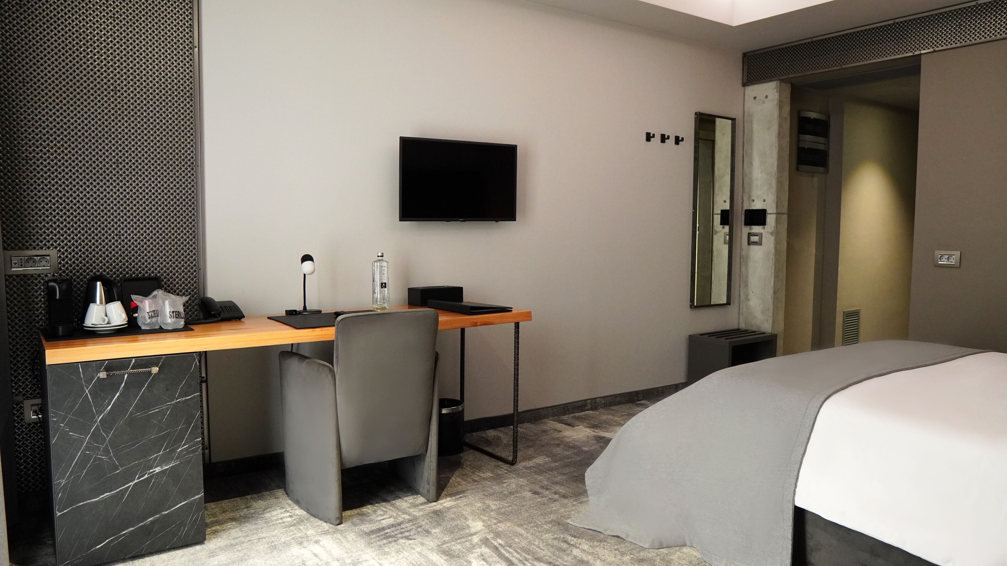 A hotel room with a bed, a desk with a computer, a chair, a TV, and a bathroom door.