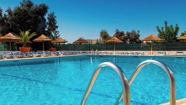 Une piscine entourée d’arbres, avec des chaises longues et des parasols.