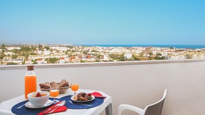 Une table dressée avec des aliments pour le petit-déjeuner et une bouteille de jus d’orange, donnant sur une ville côtière.