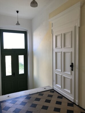Un couloir avec une porte verte, une porte blanche et un sol à carreaux.