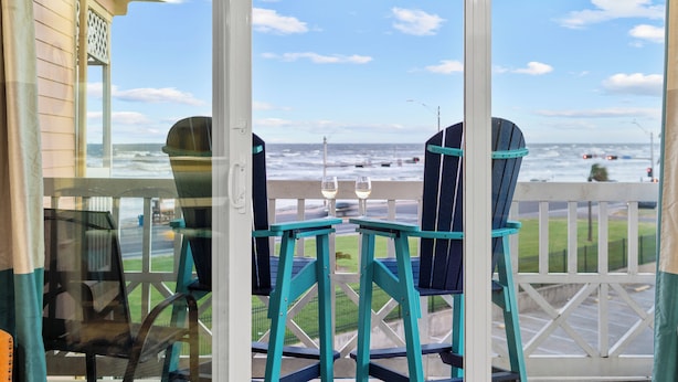 Vista desde un balcón con dos sillas y una mesa, con vista a una playa y el océano.