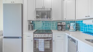 Una cocina moderna con gabinetes blancos, un refrigerador de acero inoxidable, horno empotrado y cafetera.