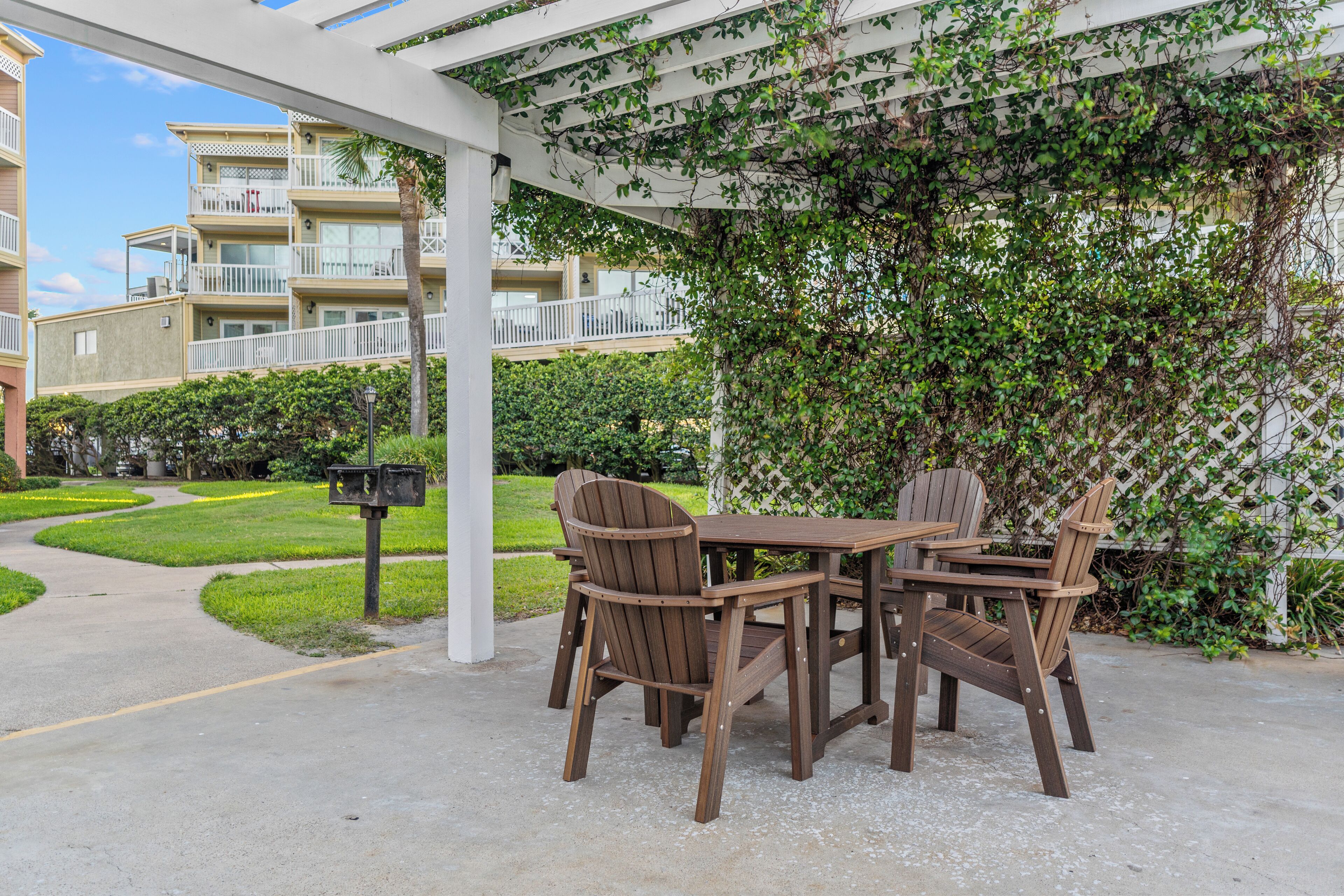 An outdoor patio with wooden furniture, a pergola, and a view of a residential building with balconies.