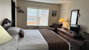 Habitación de hotel con cama, escritorio con lámpara, silla, televisor y ventana con persianas.