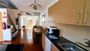 A narrow kitchen with a black countertop, a sink, and wooden cabinets. There is a fire extinguisher mounted on the wall and a ceiling light fixture. - Villa Bella 200 meters from Falésia Beach by Urban Hypotenuse (Albufeira)