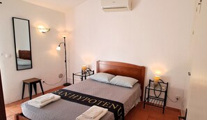 A hotel room with a bed, bedside lamps, a mirror, a bench, and a towel rack.