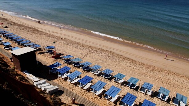 A beach with rows of blue sun loungers and a small building, likely a lifeguard station, on the sand. - Villa Bella 200 meters from Falésia Beach by Urban Hypotenuse (Albufeira)