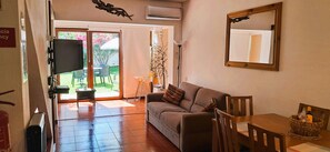A living room with a sofa, a TV mounted on the wall, a dining table with chairs, and a large mirror. - Villa Bella 200 meters from Falésia Beach by Urban Hypotenuse (Albufeira)