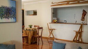 A dining area with a wooden table, chairs, and a kitchen counter with a fruit bowl. - APTO VISTA MAR MELHOR LOCALIZAÇÃO (Fortaleza)