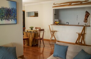 Uma área de refeições com uma mesa de madeira, cadeiras e bancada da cozinha com uma fruteira.