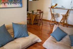 Sala de estar com um sofá bege, dois travesseiros azuis e uma mesa de jantar de madeira com cadeiras.