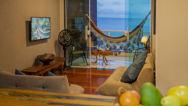 A living room with a hammock, a television, and a view of the ocean. - APTO VISTA MAR MELHOR LOCALIZAÇÃO (Fortaleza)