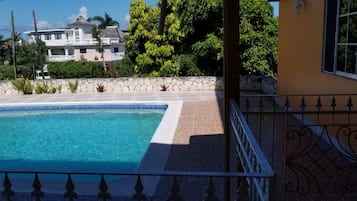 Una piscina con borde de piedra, un muro de piedra y una casa grande al fondo.