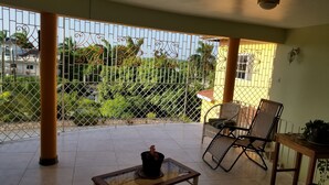 A covered balcony with a glass-top table, wicker chairs, and a potted plant. - Holiday House at Villa Montego (Montego Bay)