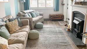 A cozy living room with a beige sofa, a patterned rug, and a fireplace. - 2 bedroom accommodation in Combe Martin (Combe Martin)