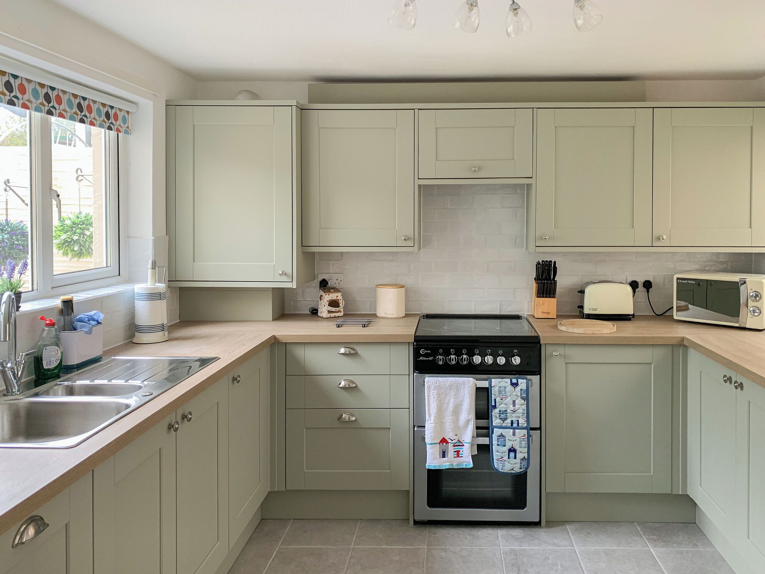 A kitchen with light green cabinets, a stainless steel sink, a stove, a microwave, and a toaster.