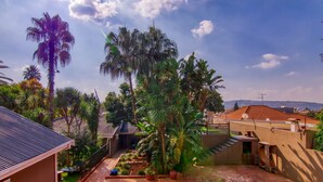 A courtyard with a brick pathway, palm trees, and a view of a distant hill.