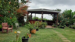 A garden with a wooden gazebo, potted plants, a wooden chair, and a small table.