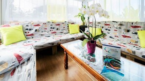 A cozy room with a wooden ceiling, a sofa with a patterned cover, a glass coffee table, and a potted plant.