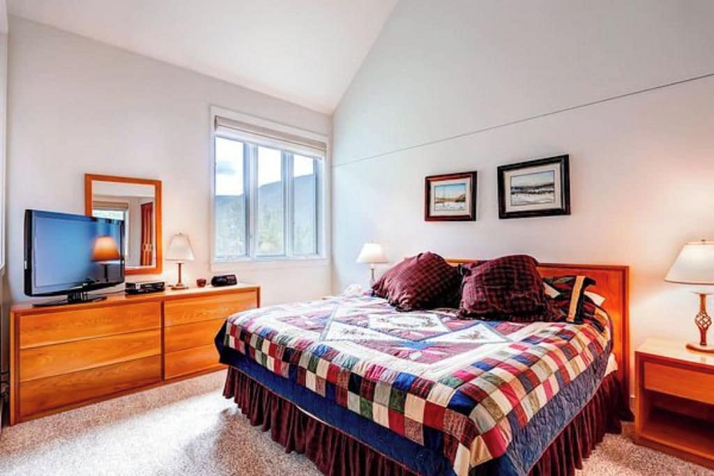A bedroom with a bed, a television, a dresser, and a window.