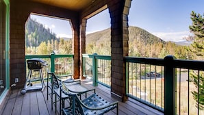 A wooden deck with outdoor seating and a view of a forested mountain range. - Soda Springs 3 Bedroom Townhome (Keystone)