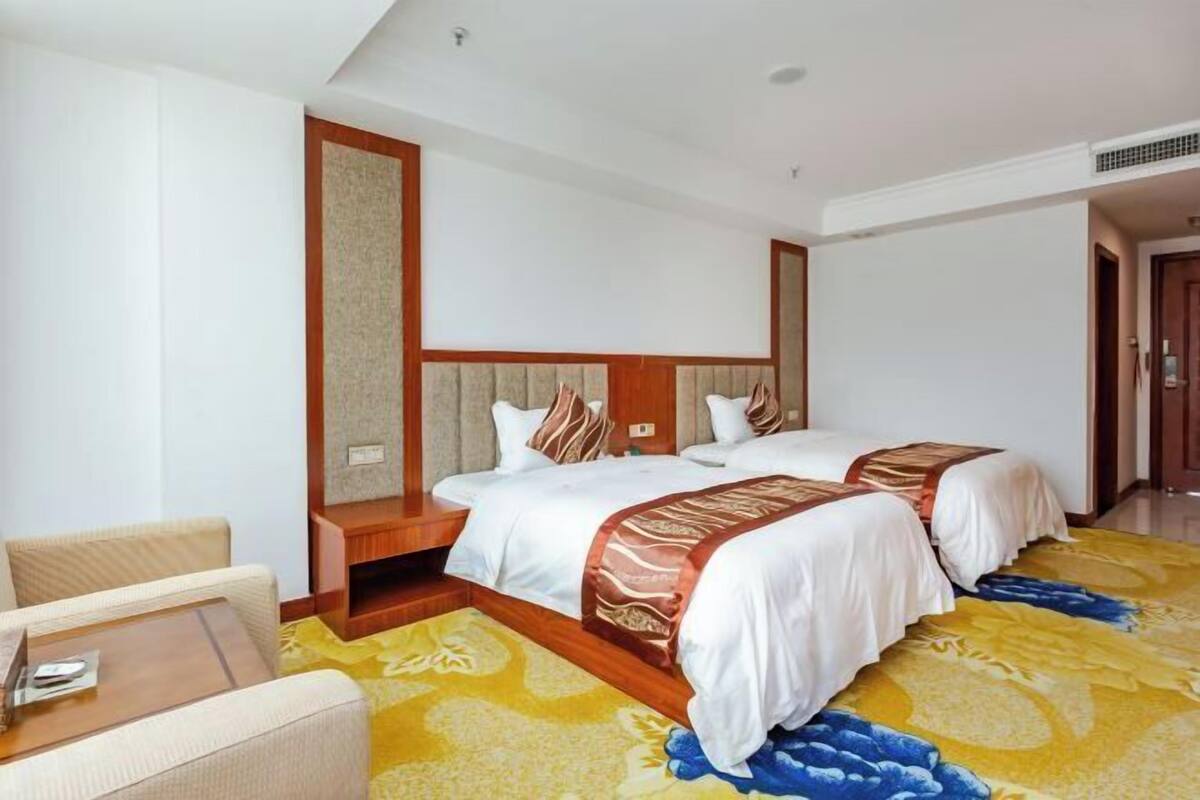 A hotel room with two beds, a sofa, and a wooden nightstand.