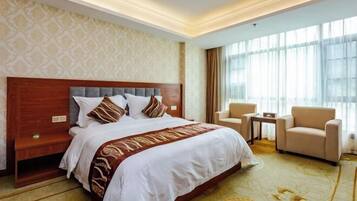 A hotel room with a large bed, a wooden headboard, a small table, two chairs, and a large window with curtains.