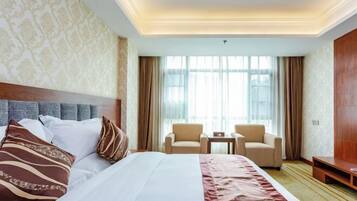 A hotel room with a large bed, two chairs, a small table, and a large window with curtains.