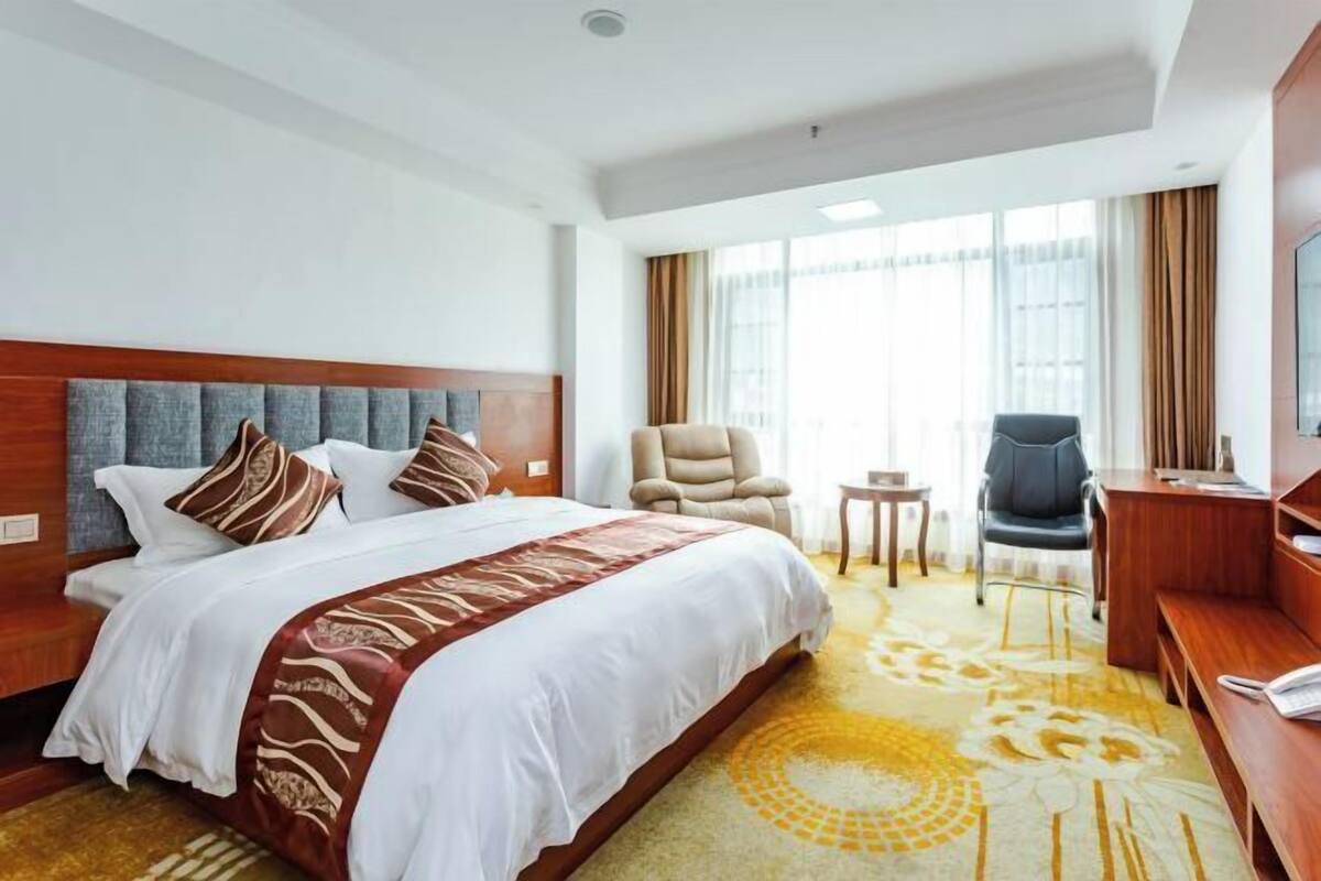 A hotel room with a large bed, a desk, a chair, and a TV.