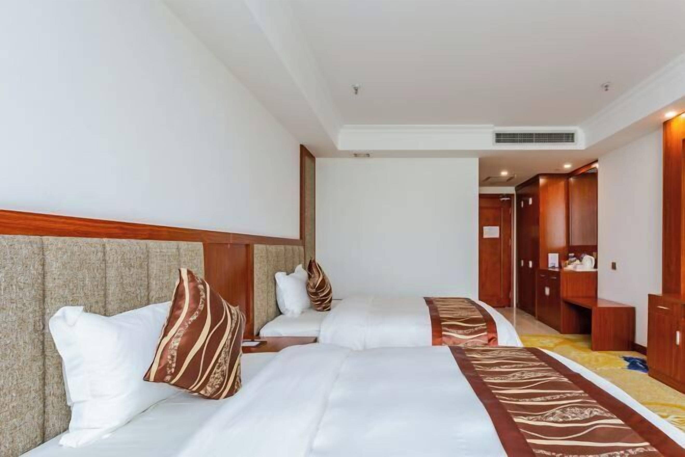 A hotel room with two beds, a wooden headboard, a carpeted floor, and a wardrobe.
