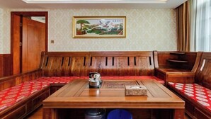 Una habitación con una zona de estar con banca de madera, una mesa con hervidor y un cuadro en la pared.