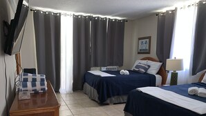 A hotel room with two beds, a TV, a bedside table, and a lamp. - Spacious apartment with sea views, everything you need to spend your vacations. (Isabela)