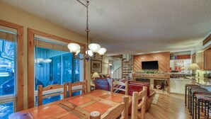 Ein großzügiger Wohnbereich mit Esstisch aus Holz, Stühlen, einem Kamin und einer Küchenzeile mit Barhocker.