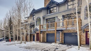 A multi-story residential building with a stone facade, large garage doors, and a covered front porch. - Northstar Townhomes in Keystone 2 Bedroom Rental (Keystone)