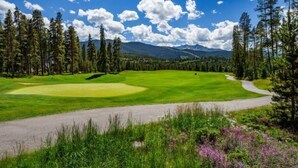 A golf course with a clear path, surrounded by tall pine trees and a mountain range in the background. - Northstar Townhomes in Keystone 2 Bedroom Rental (Keystone)