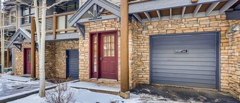 A multi-story building with stone and wood exterior, numbered garage doors, and a red door.