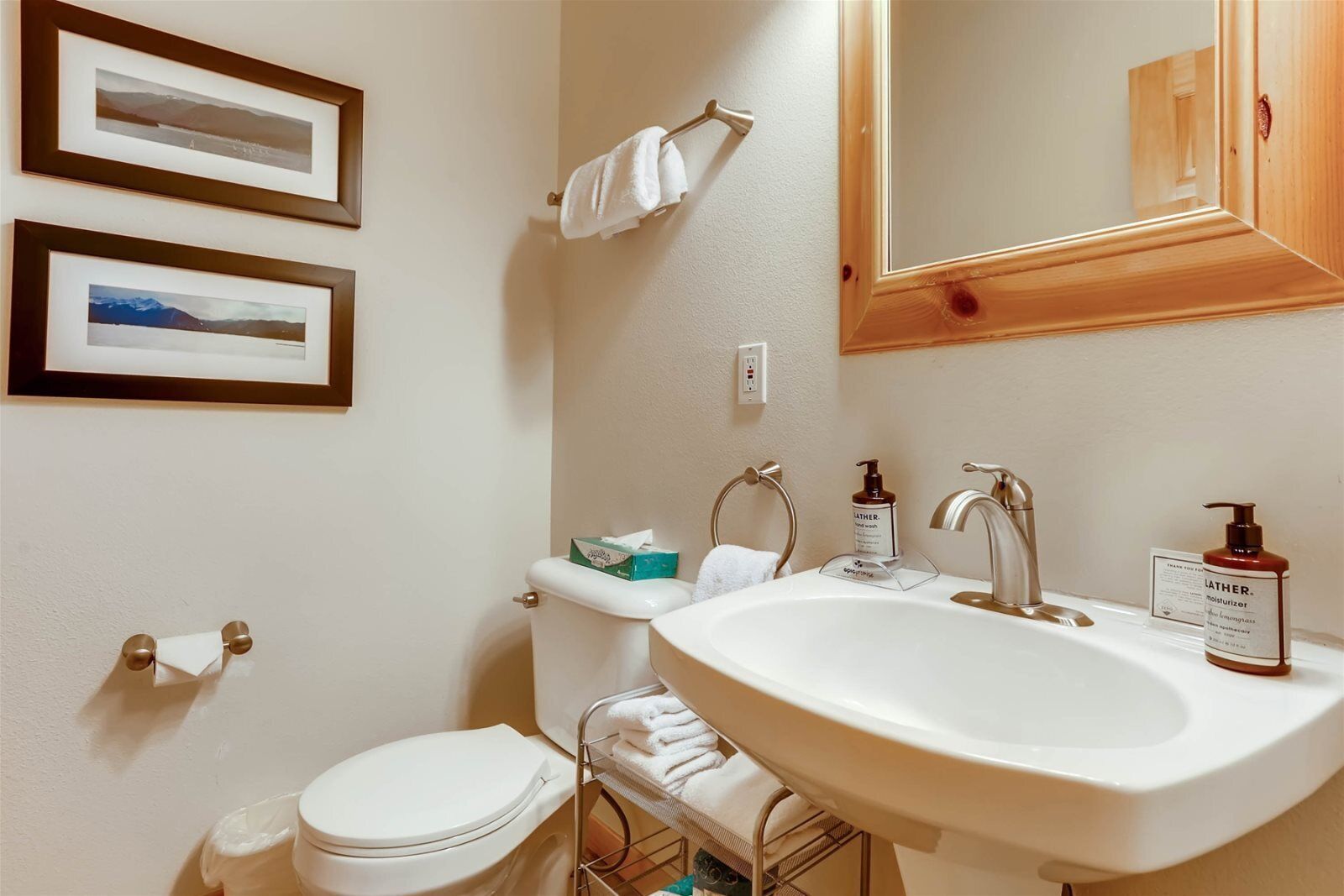 A bathroom with a white sink, two framed pictures on the wall, a toilet, and a towel rack.