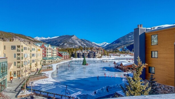 A hotel with multiple floors, a central courtyard with a frozen pond, and snow-covered mountains in the background. - Northstar Townhomes in Keystone 2 Bedroom Rental (Keystone)