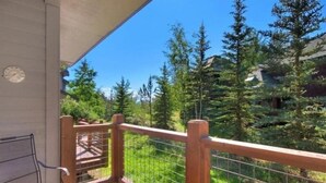 A balcony with a wooden railing, a bench, and a view of a forested area. - Northstar Townhomes in Keystone 2 Bedroom Rental (Keystone)